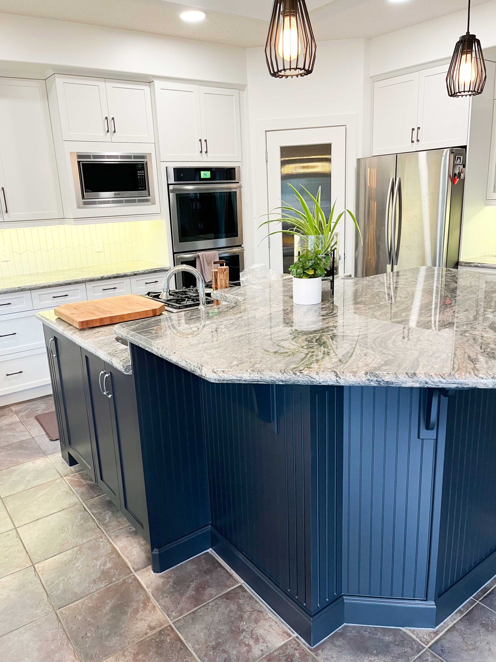 Modern kitchen featuring professionally painted white cabinets and a custom navy blue island in a Calgary home.